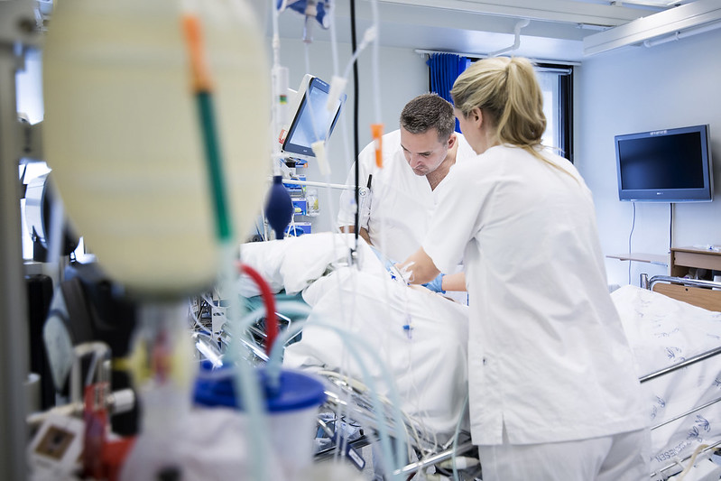 Mannlig og kvinnelig sykepleier med pasient i seng på intensivpost