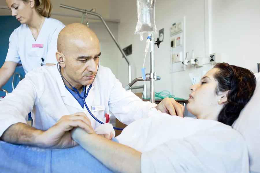 En lege som undersøker en pasient liggende i en seng