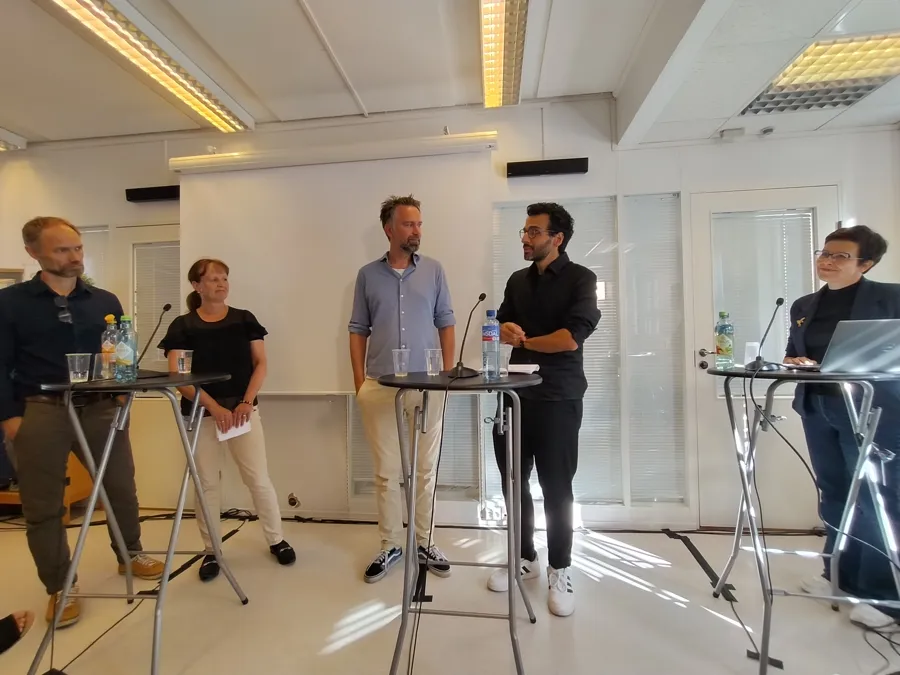 En gruppe mennesker som samtaler i et rom med bord og stoler