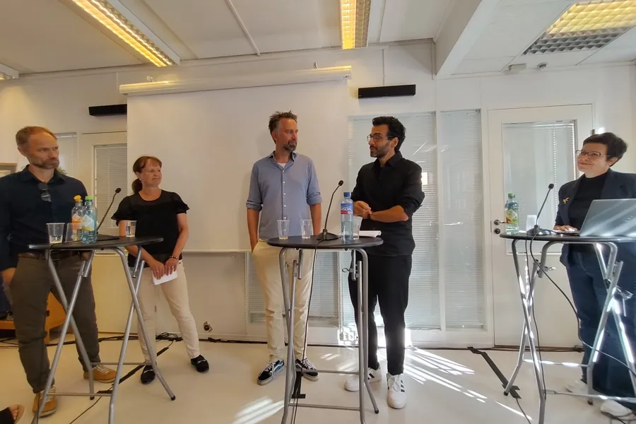 En gruppe mennesker som samtaler i et rom med bord og stoler