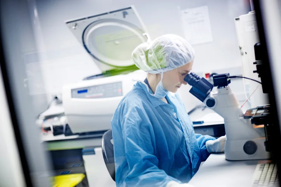En laboratorieansatt sitter foran et mikroskop