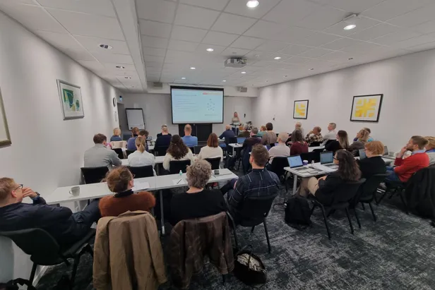 En gruppe mennesker som sitter i et rom og ser på en skjerm