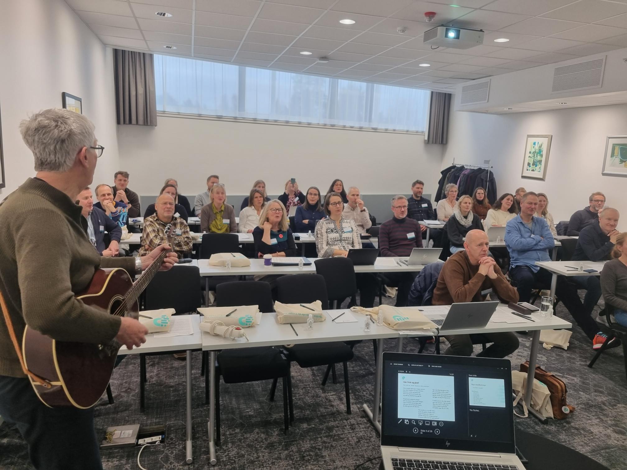 En person med gitar som henvender seg til en gruppe mennesker