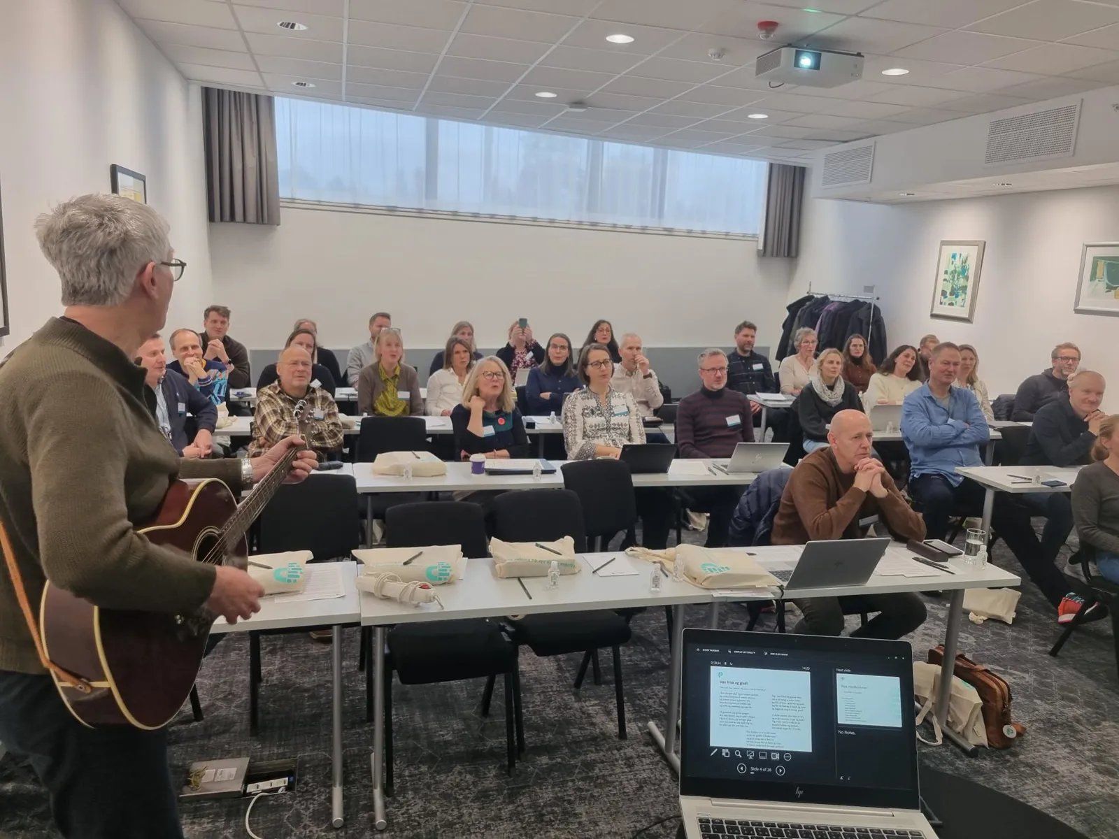 En person med gitar som henvender seg til en gruppe mennesker