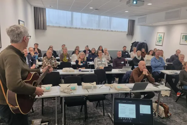 En person med gitar som henvender seg til en gruppe mennesker