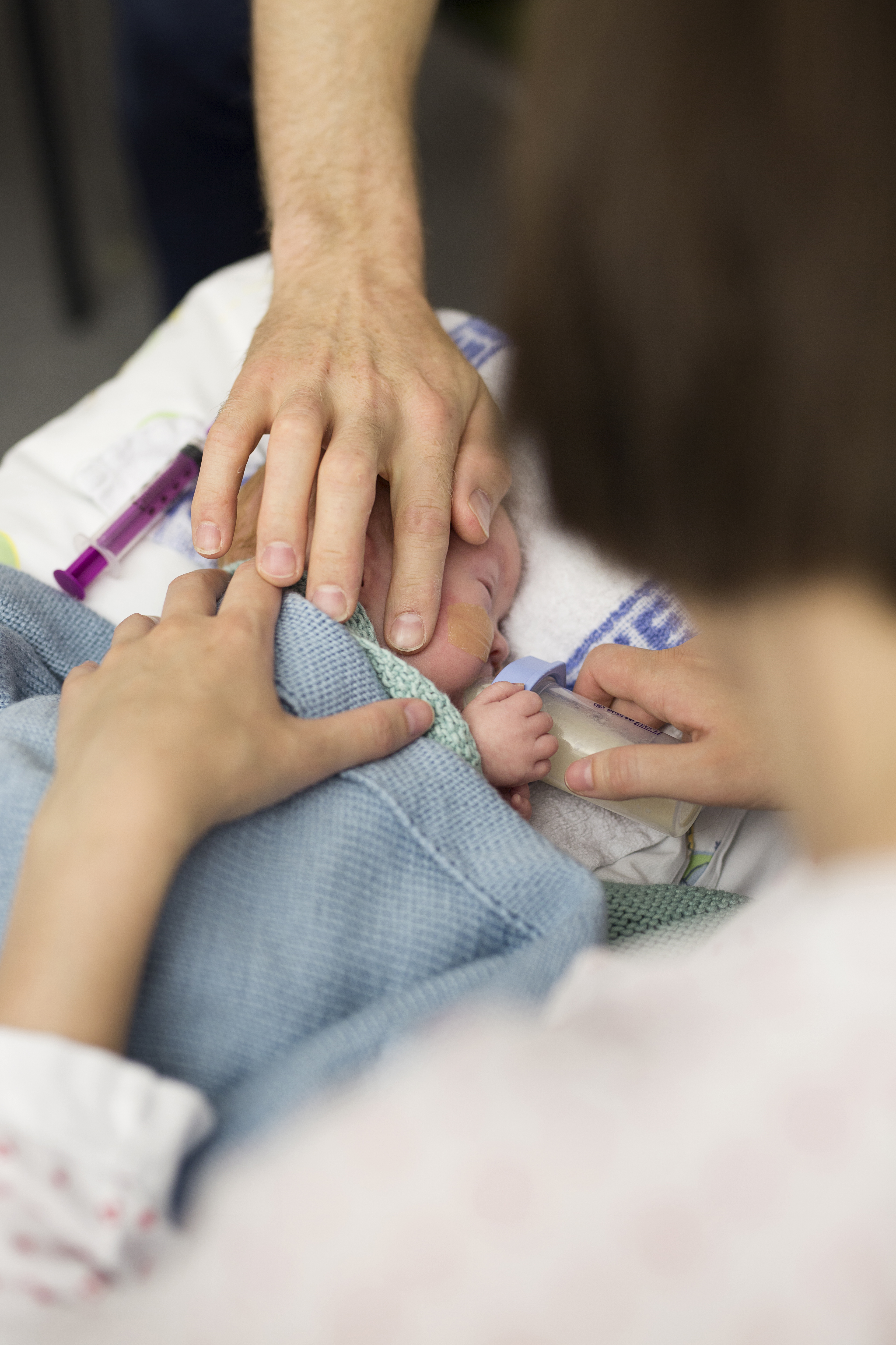 Spedbarn i seng som får flaske og omsluttes av hender